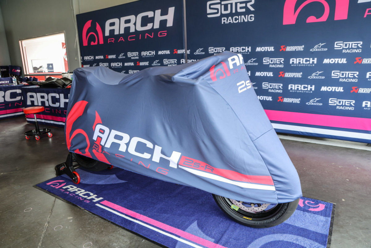 ARCH Motorcycle covered with a blue Arch Racing protective bike cover in a branded area.