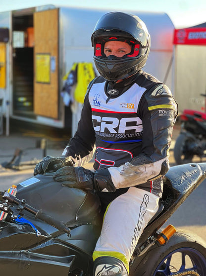 Person in racing gear sitting on a motorcycle with visible branding