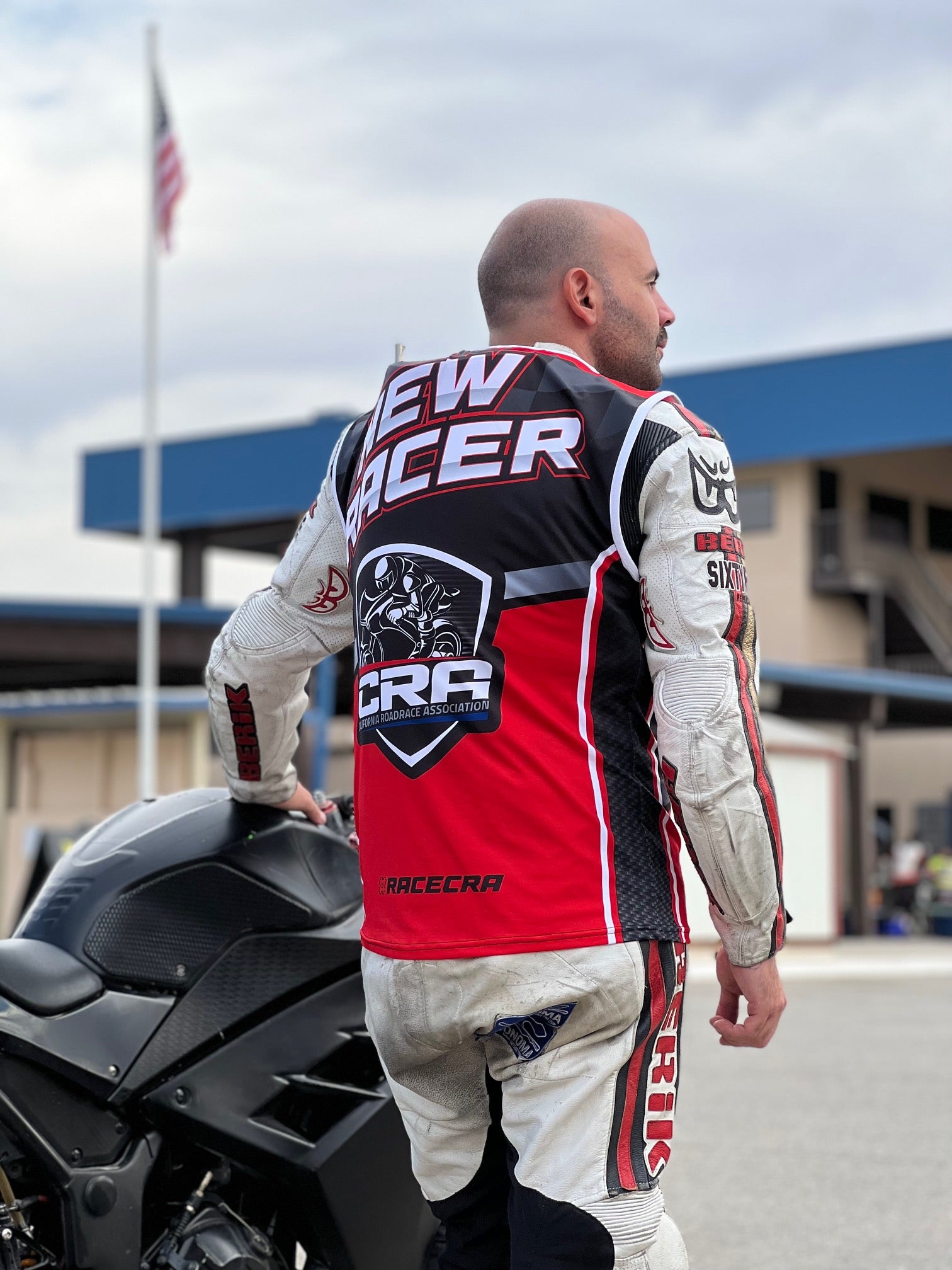 Man in racing gear standing next to a motorcycle with visible branding.