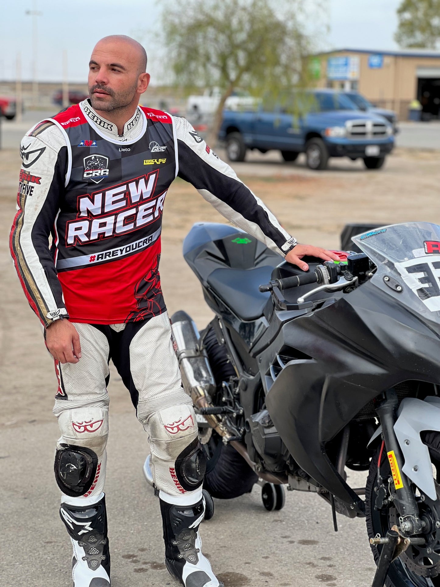 Man in racing gear standing next to a motorcycle in an outdoor setting