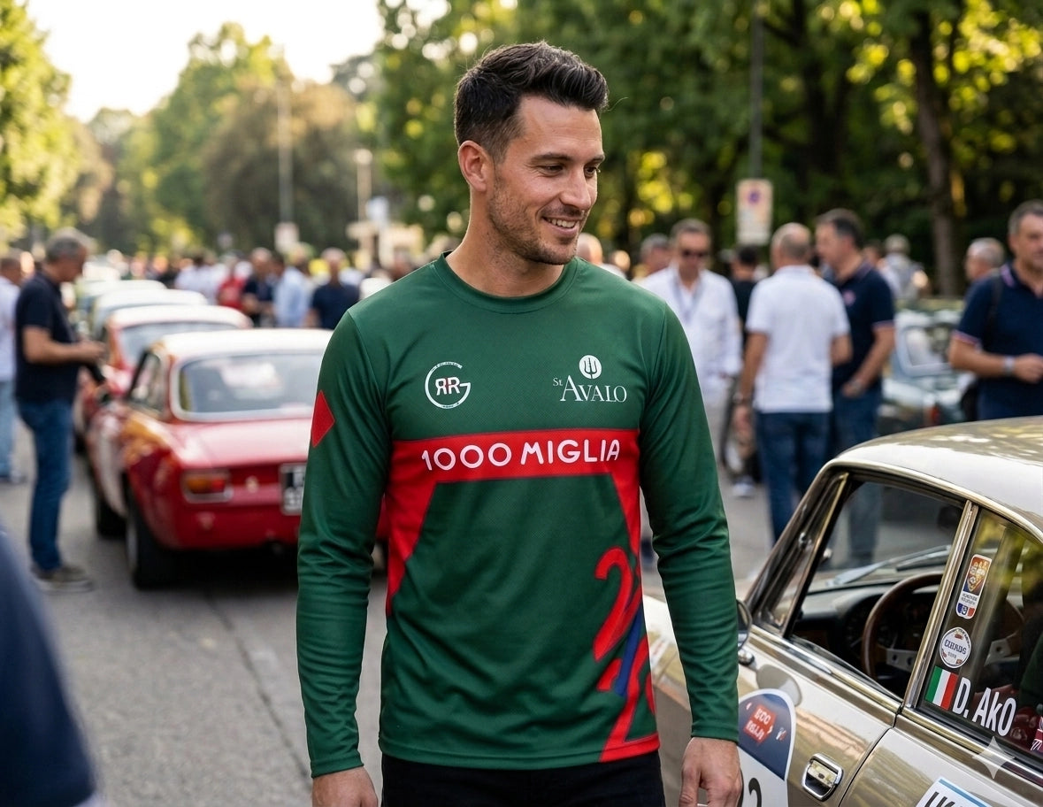 Man in a green and red racing jersey standing next to vintage cars at an event.